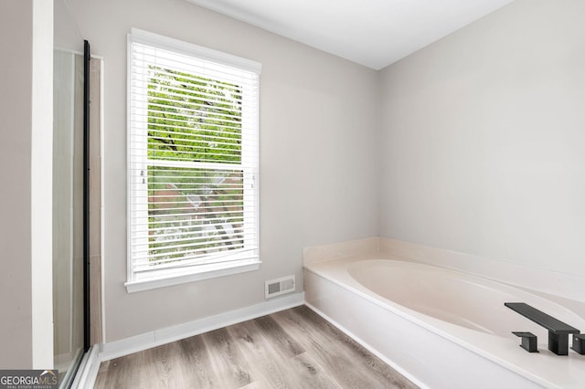 bathroom with a bath, baseboards, wood finished floors, and visible vents