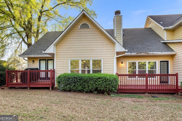 rear view of property with a yard, a shingled roof, a chimney, and a deck