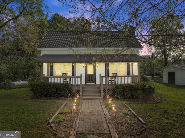 back of house with a porch, an outdoor structure, a lawn, and metal roof