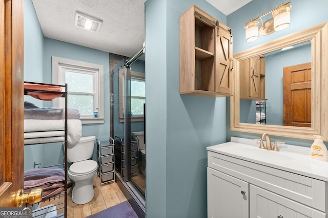 bathroom featuring vanity, visible vents, toilet, wood finished floors, and a stall shower