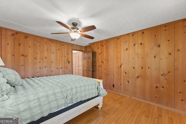 bedroom featuring a textured ceiling, a ceiling fan, wood walls, baseboards, and hardwood / wood-style flooring