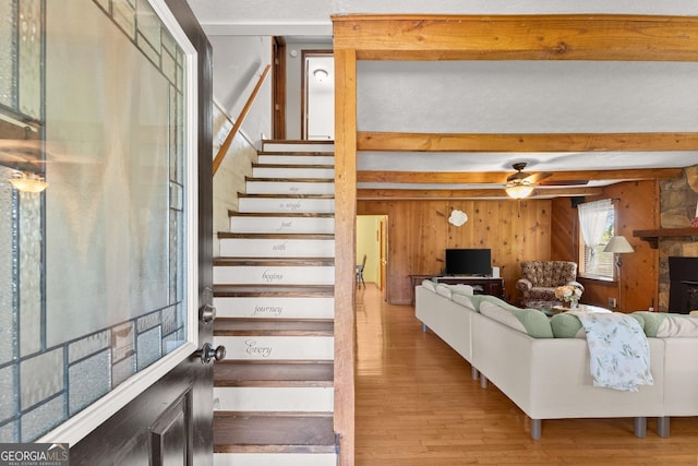 staircase with wooden walls, a ceiling fan, beam ceiling, and wood finished floors