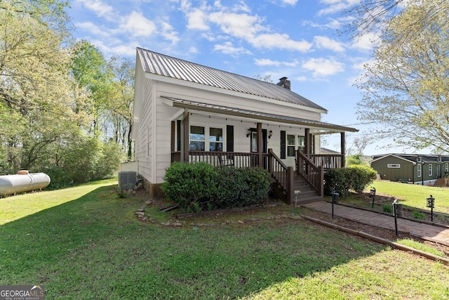 view of front of house with a porch, metal roof, a chimney, cooling unit, and a front lawn