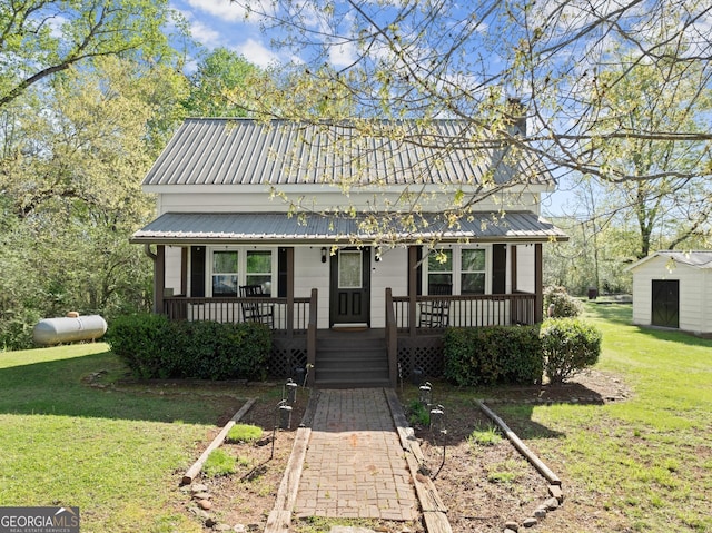 view of front of home with a porch, metal roof, a front yard, and an outdoor structure