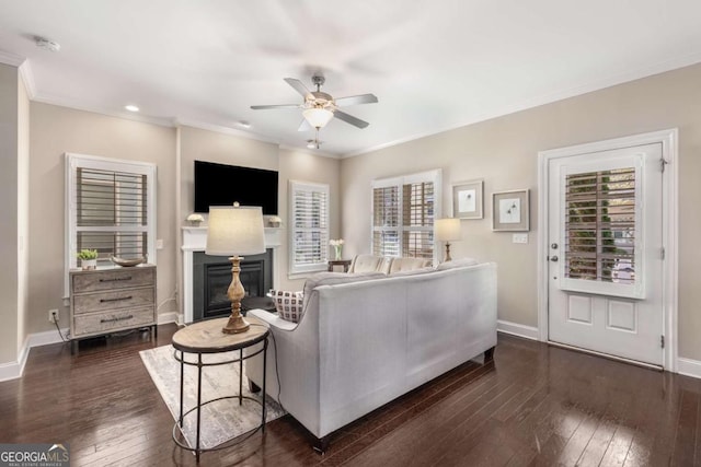 living room featuring dark wood-type flooring, baseboards, ornamental molding, and ceiling fan