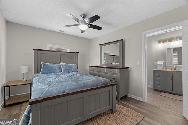 bedroom with a textured ceiling, light wood-style flooring, visible vents, and a sink