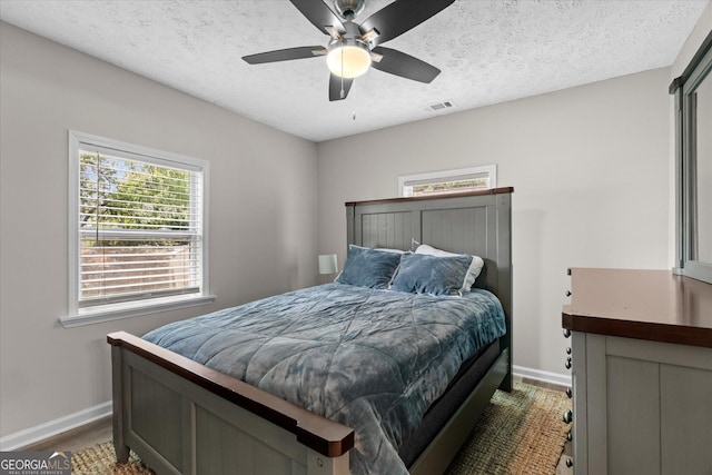 bedroom with a textured ceiling, visible vents, baseboards, and dark wood-style floors