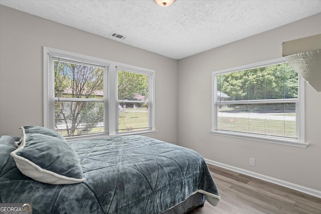 bedroom featuring wood finished floors, baseboards, visible vents, and multiple windows