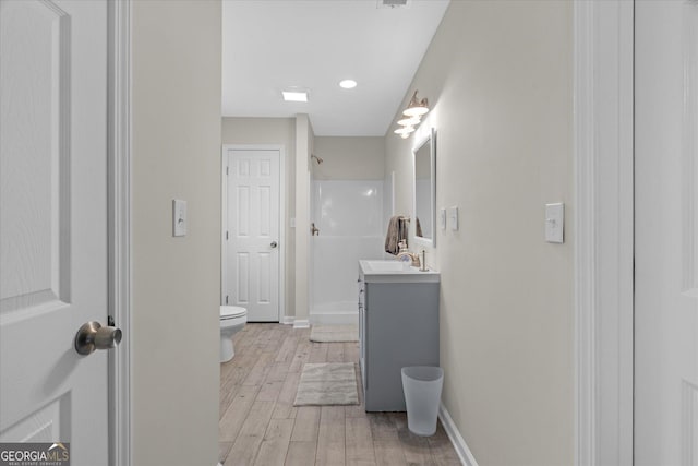 bathroom with toilet, wood finished floors, a shower, baseboards, and vanity