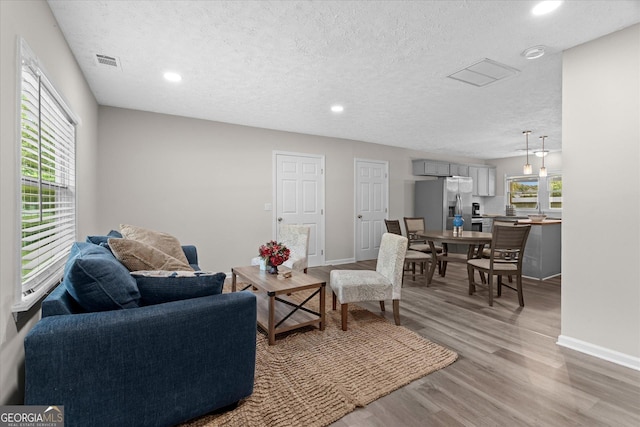 living room featuring baseboards, light wood-style floors, visible vents, and a textured ceiling