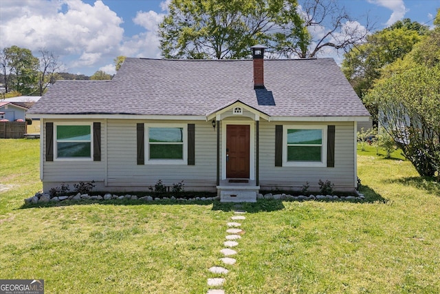 bungalow-style home with a shingled roof, a front lawn, and a chimney