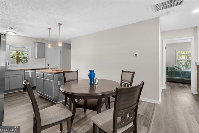 dining space with baseboards, visible vents, a textured ceiling, and wood finished floors