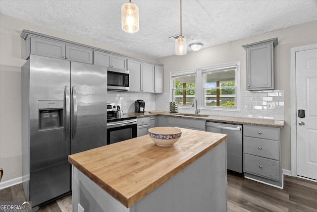 kitchen with a sink, stainless steel appliances, wood counters, and gray cabinets