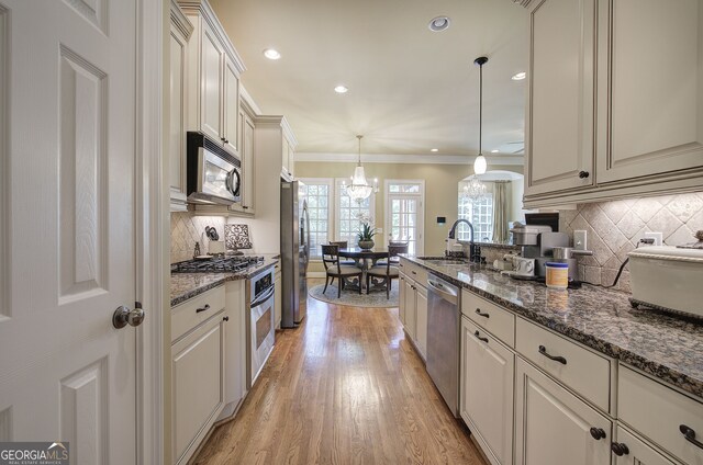 kitchen featuring crown molding, light wood-style floors, decorative backsplash, stainless steel appliances, and a sink