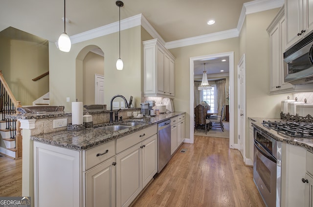 kitchen featuring stainless steel appliances, light wood-style flooring, a sink, and dark stone counters
