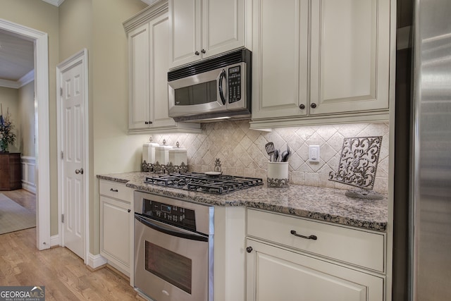 kitchen with light wood-type flooring, ornamental molding, light stone counters, decorative backsplash, and stainless steel appliances