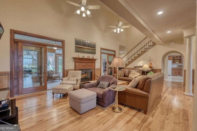 living area with arched walkways, light wood-style floors, a glass covered fireplace, ceiling fan, and a towering ceiling