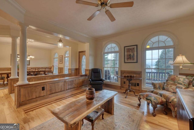 living room with decorative columns, a wainscoted wall, light wood-type flooring, ornamental molding, and a ceiling fan