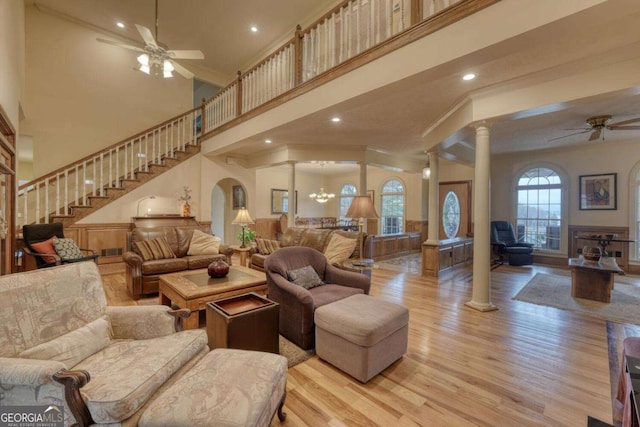 living area with a ceiling fan, ornate columns, ornamental molding, light wood-style flooring, and stairs