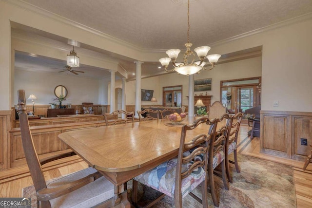 dining space featuring ornamental molding, wood finished floors, wainscoting, decorative columns, and a chandelier