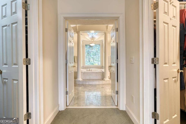 corridor featuring carpet floors, baseboards, and decorative columns