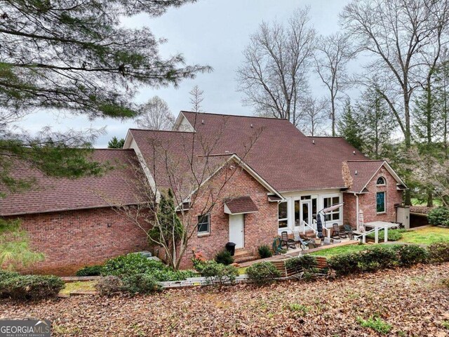 view of front of property with brick siding, a patio, and a shingled roof