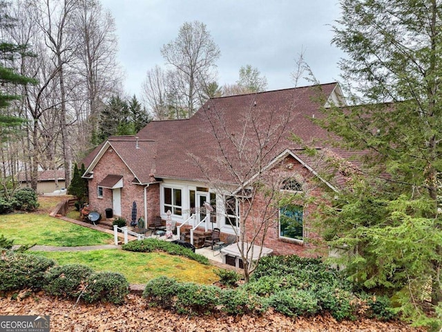 view of front facade featuring a patio area, brick siding, a front yard, and a shingled roof