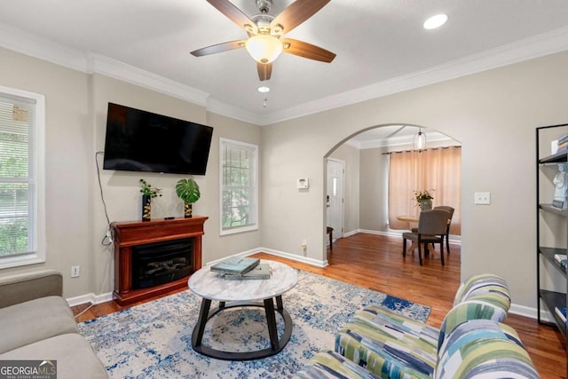 living room featuring arched walkways, wood finished floors, baseboards, ceiling fan, and ornamental molding