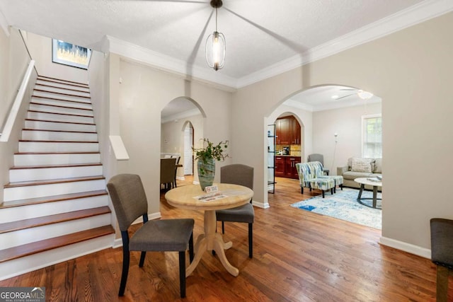 dining space with arched walkways, wood finished floors, baseboards, and ornamental molding