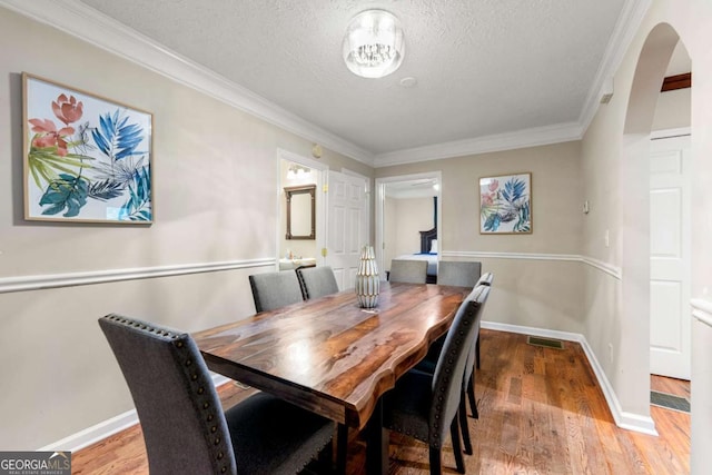 dining space with arched walkways, wood finished floors, crown molding, baseboards, and a textured ceiling