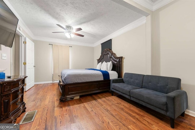 bedroom with wood finished floors, ornamental molding, ceiling fan, a textured ceiling, and baseboards