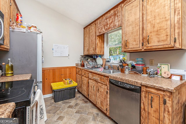 kitchen featuring appliances with stainless steel finishes, wainscoting, lofted ceiling, stone finish flooring, and a sink