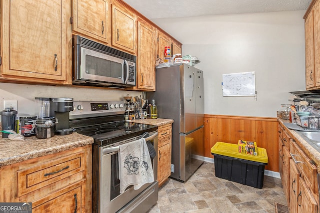 kitchen with wooden walls, stone finish floor, wainscoting, visible vents, and appliances with stainless steel finishes