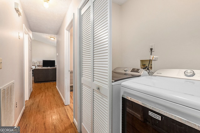 laundry area with light wood-type flooring, a textured ceiling, visible vents, washer and dryer, and baseboards