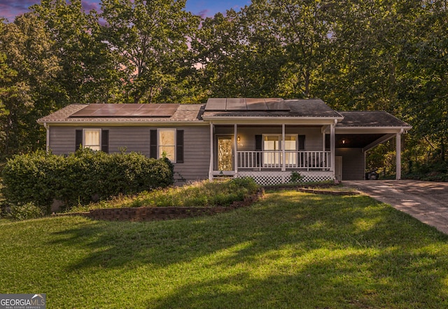 single story home with concrete driveway, a porch, an attached carport, and a lawn