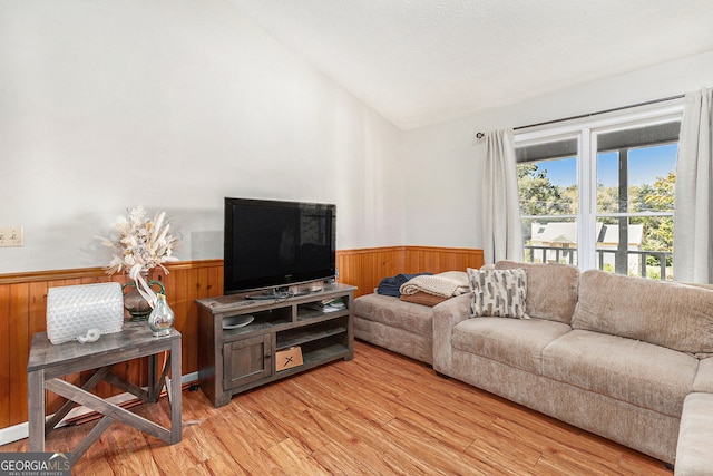 living area featuring light wood-style flooring, lofted ceiling, and a wainscoted wall