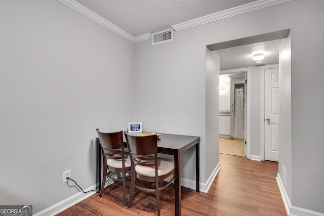 dining space with baseboards, a textured ceiling, crown molding, visible vents, and wood finished floors
