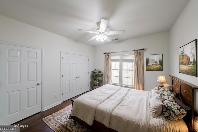 bedroom with a closet, baseboards, dark wood finished floors, visible vents, and ceiling fan