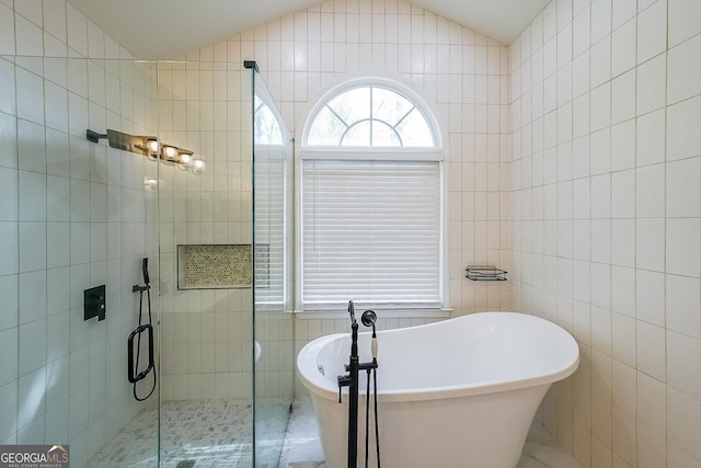 full bathroom featuring a soaking tub, tile walls, a stall shower, and lofted ceiling