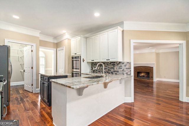 kitchen with a sink, appliances with stainless steel finishes, ornamental molding, white cabinets, and light stone countertops