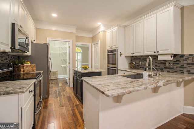 kitchen with appliances with stainless steel finishes, a sink, white cabinets, light stone countertops, and ornamental molding