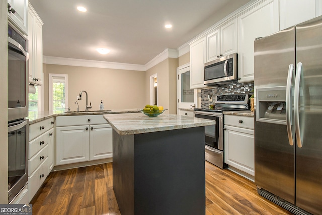 kitchen featuring appliances with stainless steel finishes, ornamental molding, a center island, a sink, and backsplash