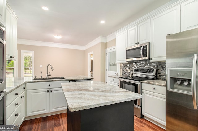 kitchen with appliances with stainless steel finishes, a sink, ornamental molding, a peninsula, and white cabinets