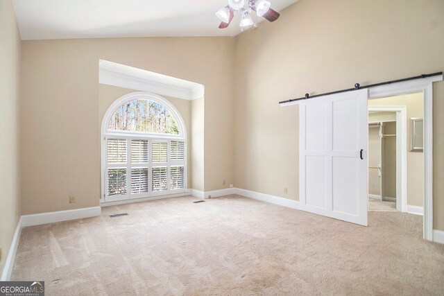 unfurnished bedroom featuring a barn door, carpet floors, a spacious closet, baseboards, and high vaulted ceiling