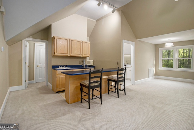kitchen featuring light brown cabinetry, light carpet, rail lighting, a kitchen bar, and high vaulted ceiling