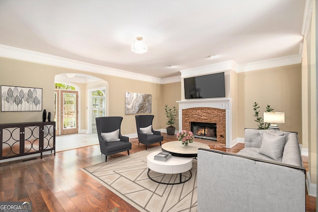 living room featuring arched walkways, a stone fireplace, wood finished floors, crown molding, and baseboards