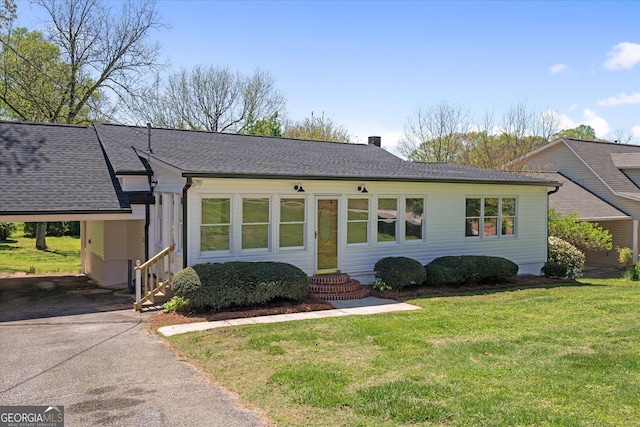 single story home with entry steps, a carport, a front lawn, driveway, and roof with shingles