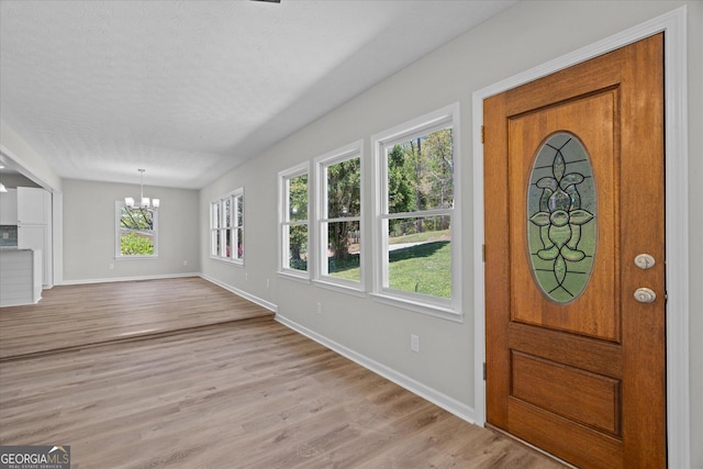 entrance foyer featuring light wood-type flooring, a notable chandelier, baseboards, and a textured ceiling
