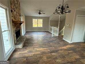 unfurnished living room with ceiling fan with notable chandelier, a fireplace, and baseboards