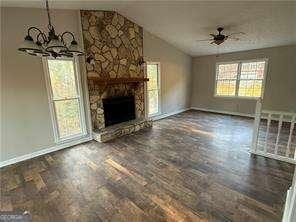 unfurnished living room with baseboards, a stone fireplace, lofted ceiling, and plenty of natural light